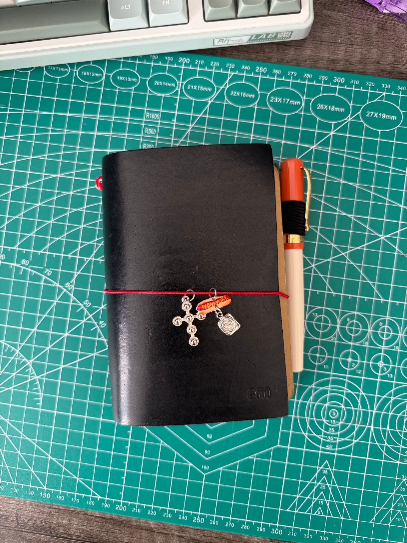 black pocket journal on a cutting mat with charms and pen